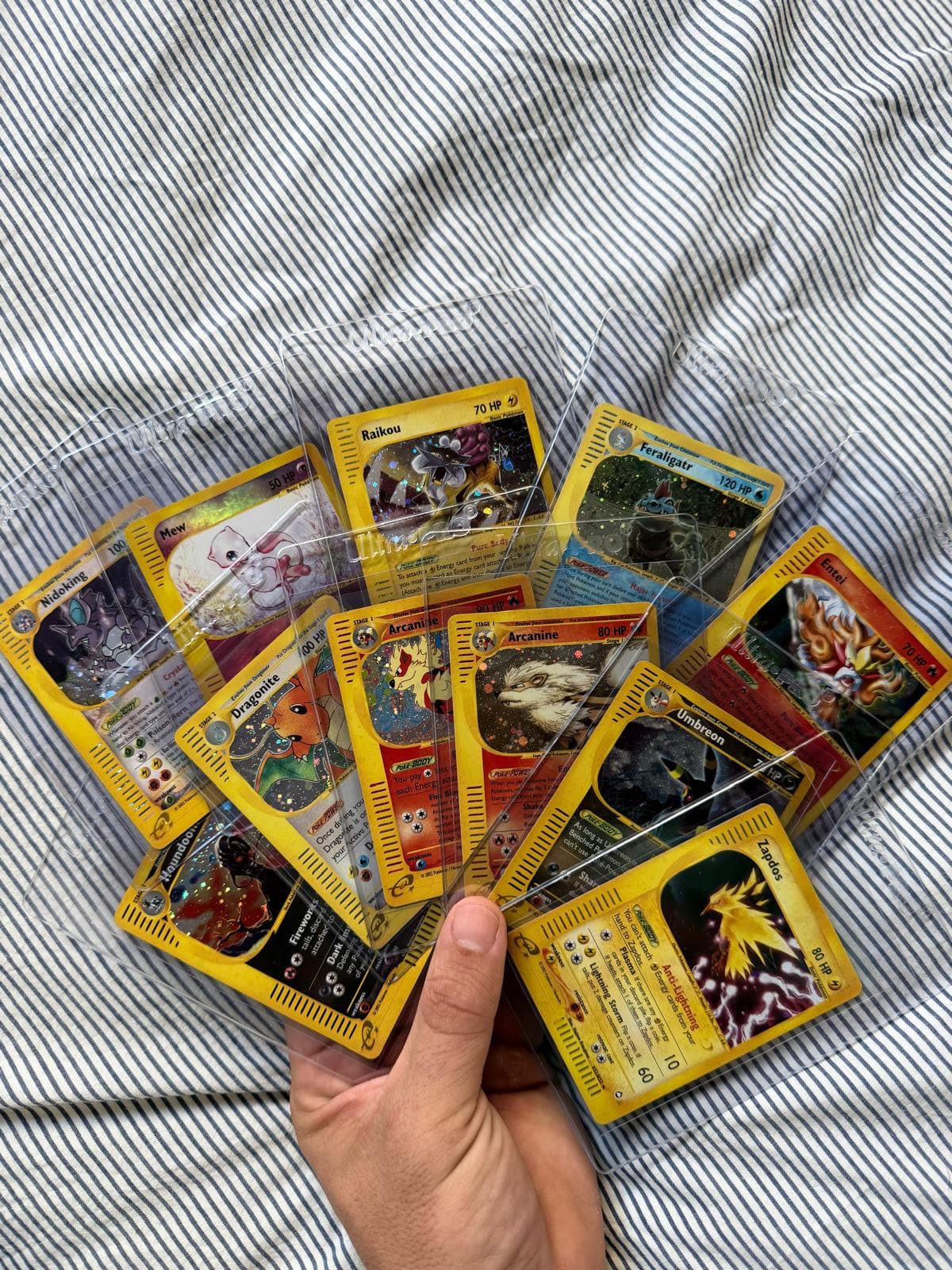 A hand holding a fanned-out spread of Pokémon cards in protective sleeves, from a real personal collection.